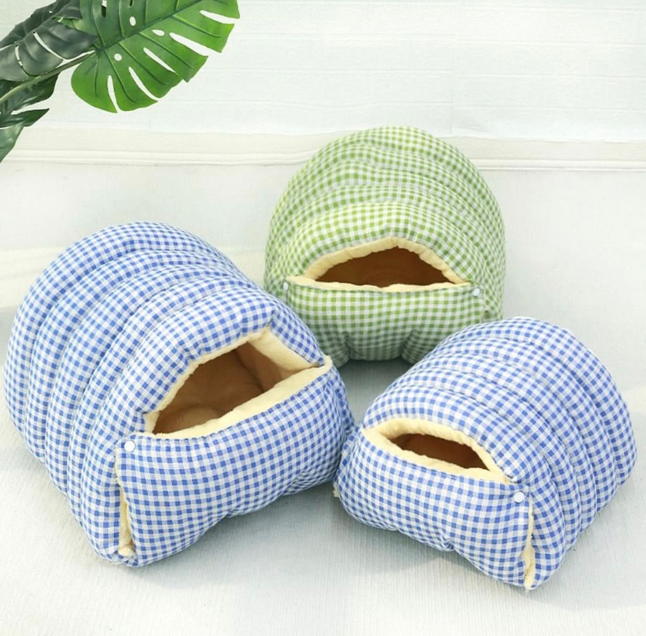 Three checkered pet houses in blue and green on a white surface with a leafy plant in the corner.