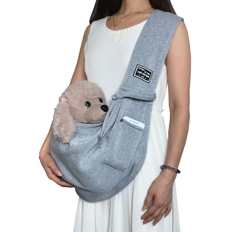 Person holding a gray pet sling with a small plush dog inside on a white background