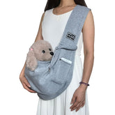 Person holding a gray pet sling with a small plush dog inside on a white background