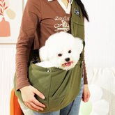 Person holding a white dog in an olive green pet sling against a neutral background