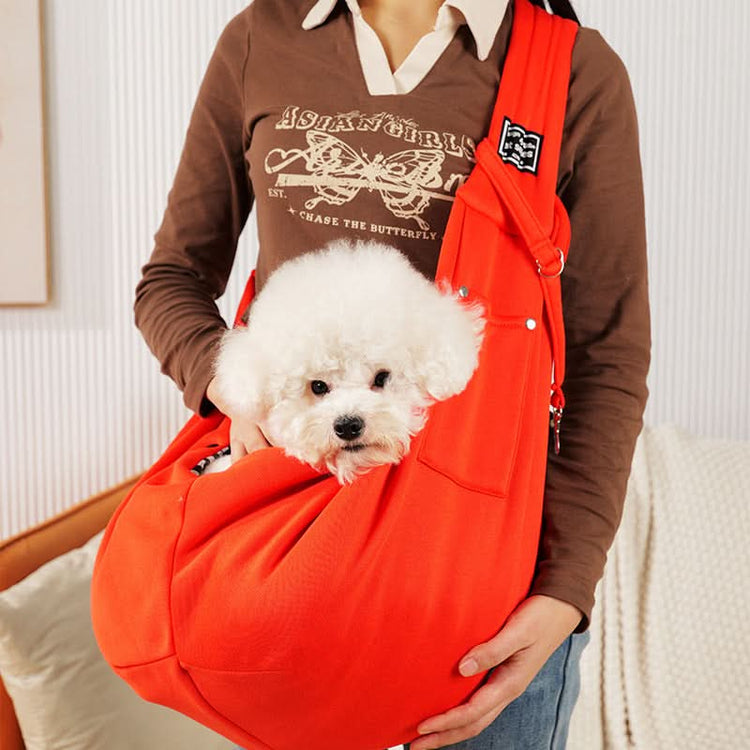 Person holding a small white dog in an orange pet sling against a neutral background