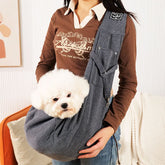 Person holding a small white dog in a gray pet sling against a neutral background