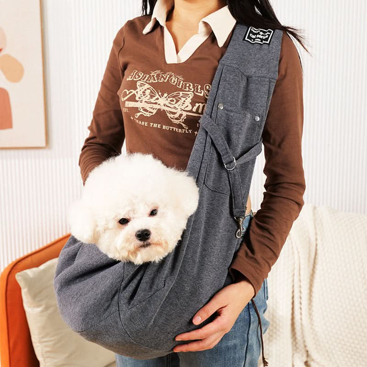 Person holding a small white dog in a gray pet sling against a neutral background
