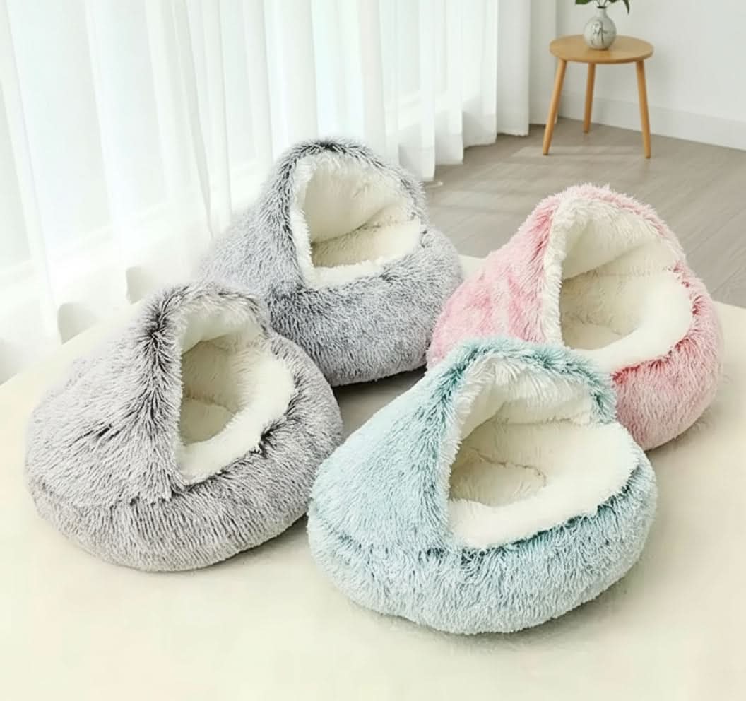 Four fluffy pet beds in gray, pink, and blue on a light surface with a blurred background.