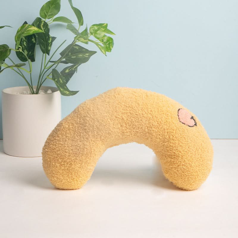 Yellow neck pillow with a face design on a light surface with a plant in the background