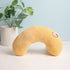 Yellow neck pillow with a face design on a light surface with a plant in the background