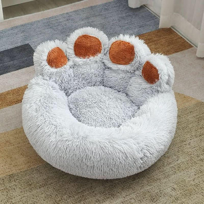 Plush paw-shaped pet bed with soft gray fur and brown paw accents on a rug