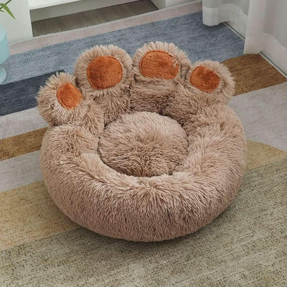 Fluffy paw-shaped pet bed in beige with orange accents, cozy for cats or dogs, on a rug