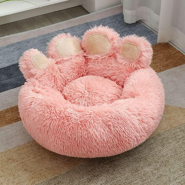 Pink plush pet bed shaped like a cat paw with soft fur and raised edges on a rug