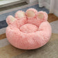 Pink plush pet bed shaped like a cat paw with soft fur and raised edges on a rug