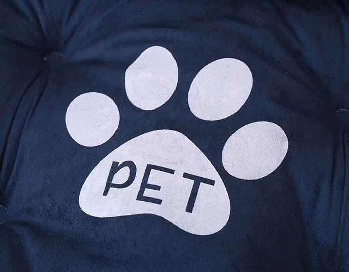 Close-up of a navy blue plush pet bed with a white paw print and the word &