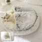 Cat sleeping in a semi-closed, fluffy grey pet bed on a soft white rug